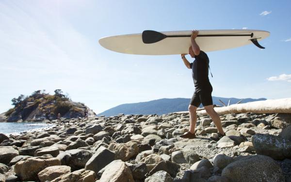 Adulte mature transportant un paddle board sur la plage vers la mer.
